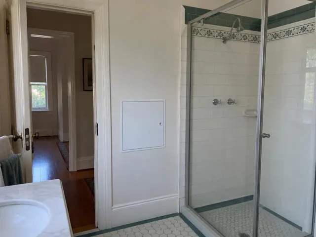 Bathroom wall with a small access panel beside a tiled shower and glass screen in Eastwood